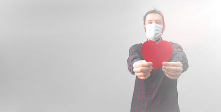 Young man in medical mask on his face holding a paper red heart in his hand. concept of valentines...