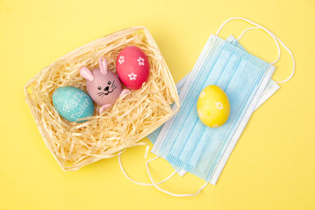 Easter Flat lay with a medical face mask, colorful painted eggs lie in the hay on a white tray....