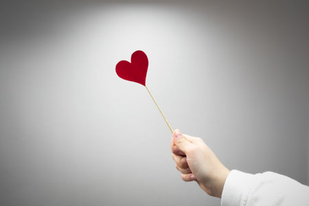 Love symbol by heart on a stick and female hand on gray backgroundの写真素材