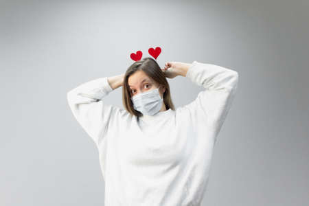 Portrait of woman in medical protective wearing mask holding in hands red hearts. concept of valentines day during pandemic period, valentine in the distanceの写真素材