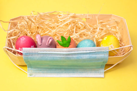 Easter Flat lay with a medical face mask, colorful eggs lie in the hay on a white tray. Holiday...