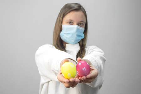Sad young woman with colored Easter eggs wearing protective medical face mask.の写真素材
