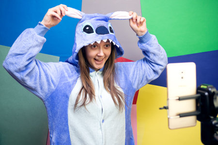 Girl blogger in kigurumi talking with followers, live streaming, looking to smartphone screen on...