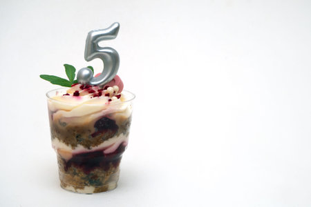 Birthday trifle cake with candle labeled number 5 on white background. portioned mini cake with copy...