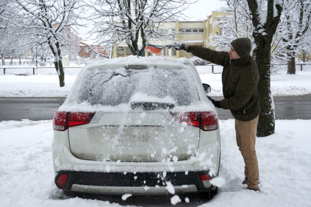 Removing snow from car with a brush. Man cleans his car after a snowstorm