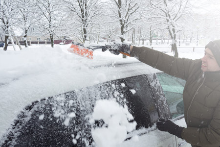 Removing snow from car with a brush. Man cleans his car after a snowstorm