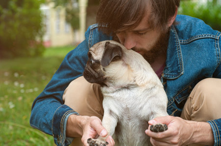 Man with his pug dog playing outdoor in the park, Young owner hugs and love his pet.の写真素材