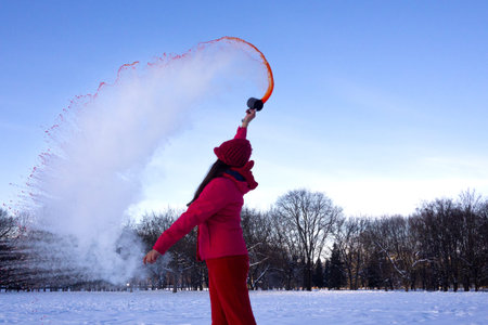 Unrecognisable person pouring hot water up in the sky, sunny winter day. Boiling water challenge,...