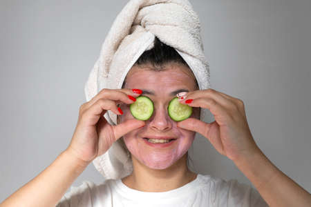 Woman with a face mask and towel on head and pieces of cucumber on her eyes. Spa and relaxing beauty procedures at homeの写真素材