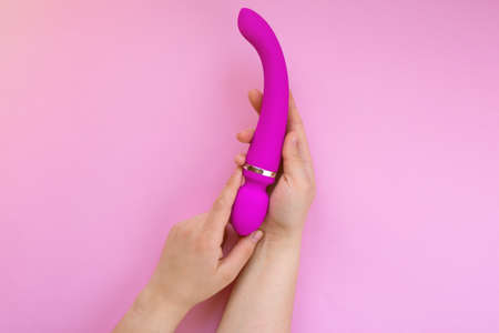 Sex toy pink vibrator in female hands on a pink background.の写真素材