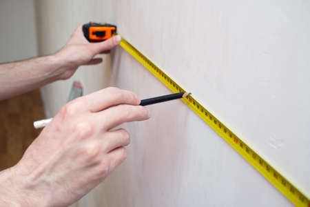 Man repair measures the white wall of the with a tape measure and before wallpapering. renovation apartment. close upの写真素材