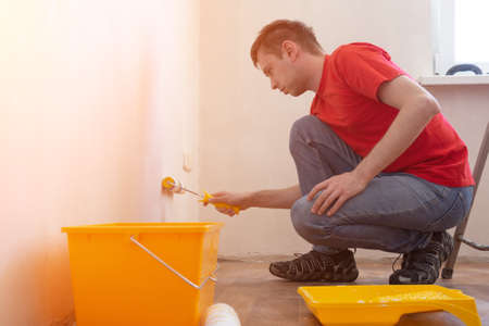 Man priming the wall with a roller. Repair of the interior. Young male decorator painting a wall in...