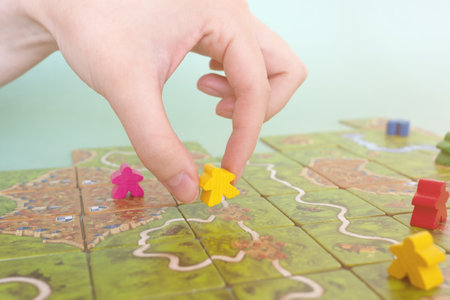 hand with chip under the playing field. Carcassonne game cards and chips on table close up. Board game and leisure concept. Minsk, Belarus - July 10, 2021のeditorial素材
