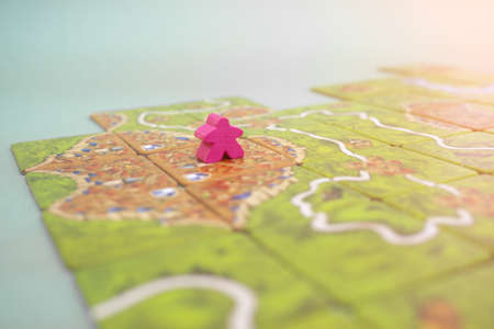 The tiles and meeples of tabletop boardgame Carcassonne with a roads and castles and river. Popular...