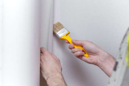 Young professional repairman glueing wallpapers on concrete wall. Repair apartment. Home renovation conceptの写真素材