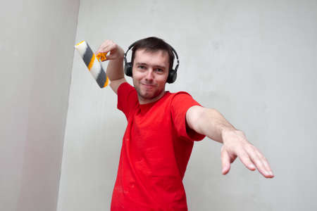 Funny Caucasian man listening to music and dancing with roller brush. Young male having fun during home repair and renovation roomの写真素材