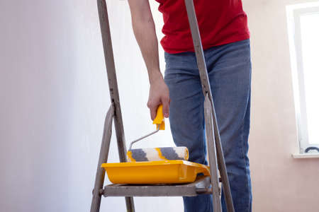 Man priming the wall with a roller. Repair of the interior. Young male decorator painting a wall in the empty room. Concept renovation do it yourselfの写真素材
