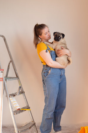 Happy woman makes repairs in her apartment with her funny pug dog. happiness in anticipation of a new home and moving. independent single life with a petの写真素材
