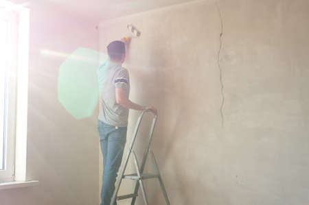Man priming the wall with a roller. Repair of the interior with copy space. Young male decorator painting a wall in the empty room. Concept renovation do it yourselfの写真素材