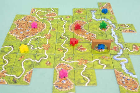 The tiles and meeples of tabletop boardgame Carcassonne with a roads and castles and river. Popular family hobby board game. Minsk, Belarus - July 10, 2021のeditorial素材