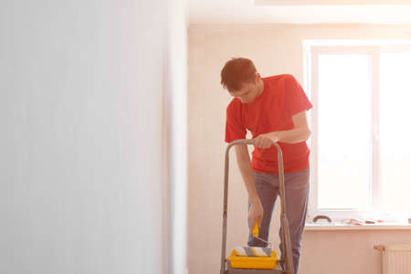 Man priming the wall with a roller. Repair of the interior. Young male decorator painting a wall in house. Concept renovation do it yourselfの写真素材