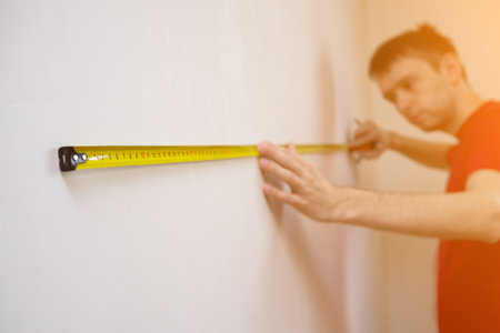 Man repair measures the white wall of the with a tape measure and before wallpapering. renovation...