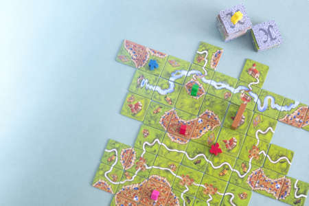 The tiles and meeples of tabletop boardgame Carcassonne with a roads and castles and river. Popular...
