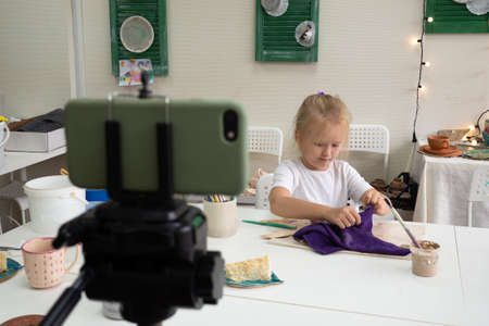 Girl vlogger recording video with modelling clay and speaking for smartphone camera. Kid blogger in a ceramic studio creating interesting content for children.の写真素材