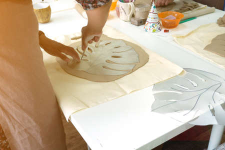 Woman hand potter making clay monstera leaf in pottery workshop studio. Process of creating ceramic...
