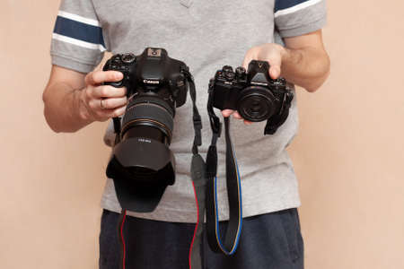 Man is holding in one hand dslr camera Canon and mirrorless Olympus in another one. Comparison of two cameras for shooting. Choosing before buying and evaluating the pros and cons of camerasのeditorial素材
