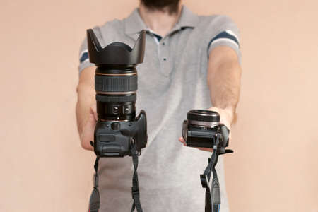 Man is holding in one hand dslr camera and mirrorless in another one. Comparison of two cameras for...