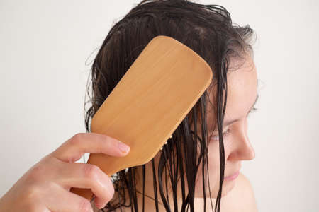 Woman brushing with combs tangled hair with conditioner after shower slow motion. Close up