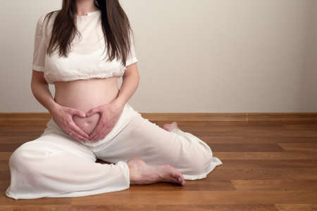 pregnant woman sitting on floor in kapotasana pose and make heart shaped hand show love. health care pregnacy concept with copy spaceの写真素材