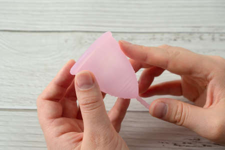 menstrual cup in hands. feminine menstruation hygiene material product on wooden background