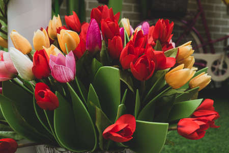 Mix of spring floral tulips in basket. Poster with fake tulips flowers petals and leaves. Womans Day and Mothers Day celebration.の写真素材