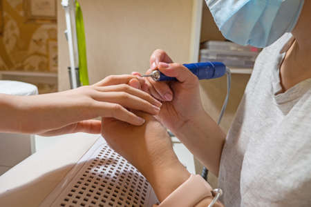 Manicurist master removing cuticles. Processing of rough cuticles and lateral folds of nails on hands with a conical instrument. Medical hardware manicure in a beauty salonの写真素材
