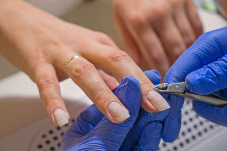 Manicurist master removing cuticles with manicure scissors. Hardware combined manicure in a beauty...