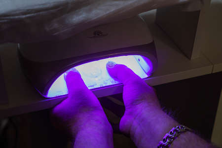 Client in manicure salon dryes gel polished nails in UV light lamp. Beauty salon and beautician appointment concept.の写真素材