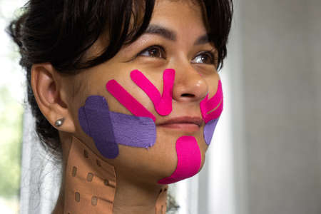 Physiotherapy of Face aesthetic taping. Portrait of woman with pasted konesiotape for rejuvenation and face tightening without surgery. Anti-wrinkle cosmetic tape.の写真素材