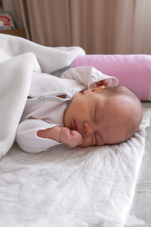 cute little newborn baby girl peacefully sleeps in the nursery on a white cotton bed. vertical