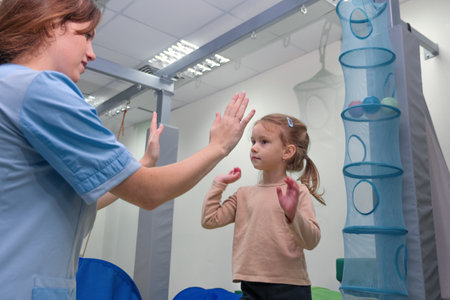 Child girl give five physiotherapist during sensory integration session. The concept of happiness and one team together. Cheerful kid and therapist celebrating teamwork at lesson.の写真素材