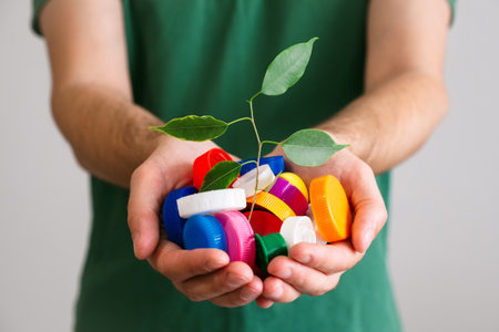 Hands holding a handful of colorful plastic lids with green leaves. Concept of environmental...