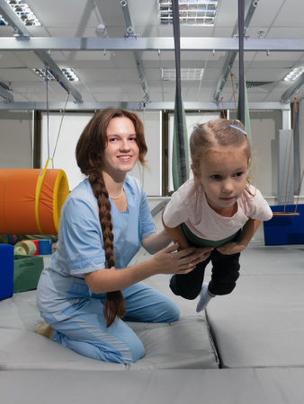 Child with physiotherapist on swing during sensory integration session. Little girl in...