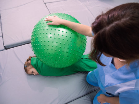 Physical therapist working with little girl in sensory room. Exercising with fitness ball and pressure to help kid relax in a therapy center. sensory integration sessionの写真素材