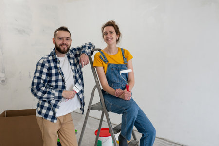 couple posing during repair works painting wall together and standing with tools. Happy family make renovation DIY renew home concept. decorating work in new apartmentの写真素材