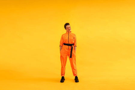Full length body size photo of happy woman wear modern orange overalls on bright yellow color background. Cheerful and energetic middle age female with colored make up having fun near copy spaceの写真素材