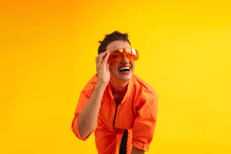 Middle age funny and Cheerful woman wear modern Orange overalls with glasses standing over yellow color background. Female having fun and energetic movement studio shotの写真素材