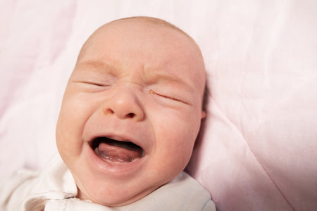 Little two month old newborn baby boy is crying. Screaming hungry infant face portrait close up....