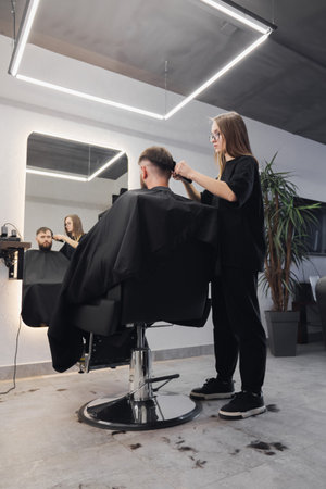 Professional woman barber wielding electric hair clipper making Fashionable haircut. Bearded Man client visit gentleman grooming beauty salon for hairstyle care. Modern Haircut style in barber shopの写真素材