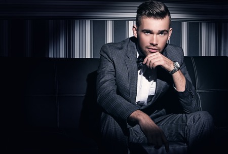 Portrait of a handsome man in a suit who sits in the spotlight over a striped background Portrait of a handsome man in a suit who sits in the spotlight over a striped background